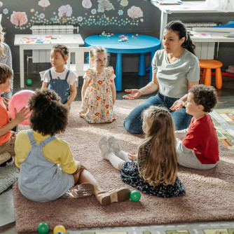 Eine Kindergruppe sitzt mit einer Erzieherin im Kreis